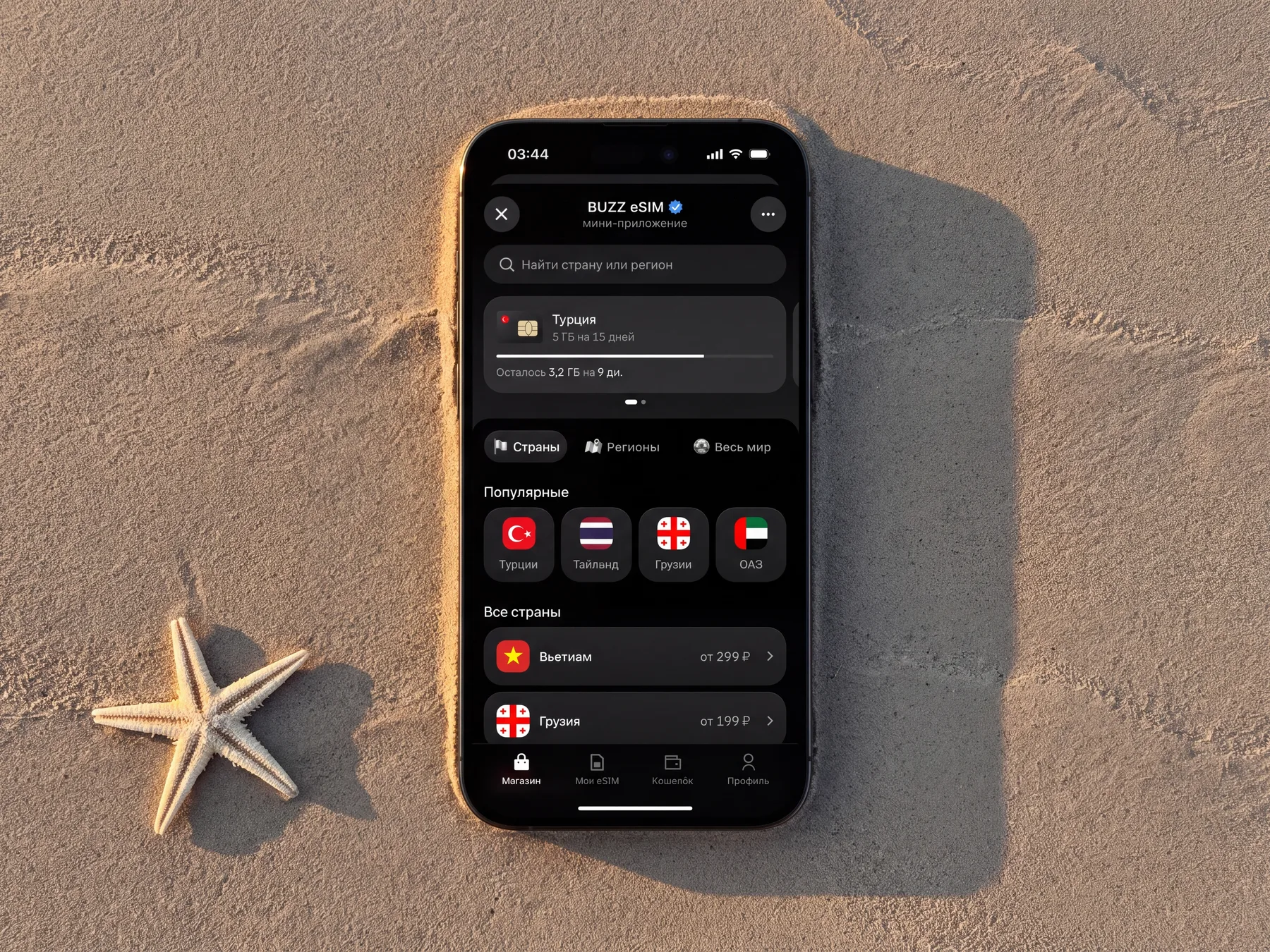 eSIM catalog on a phone lying in beach sand next to a starfish